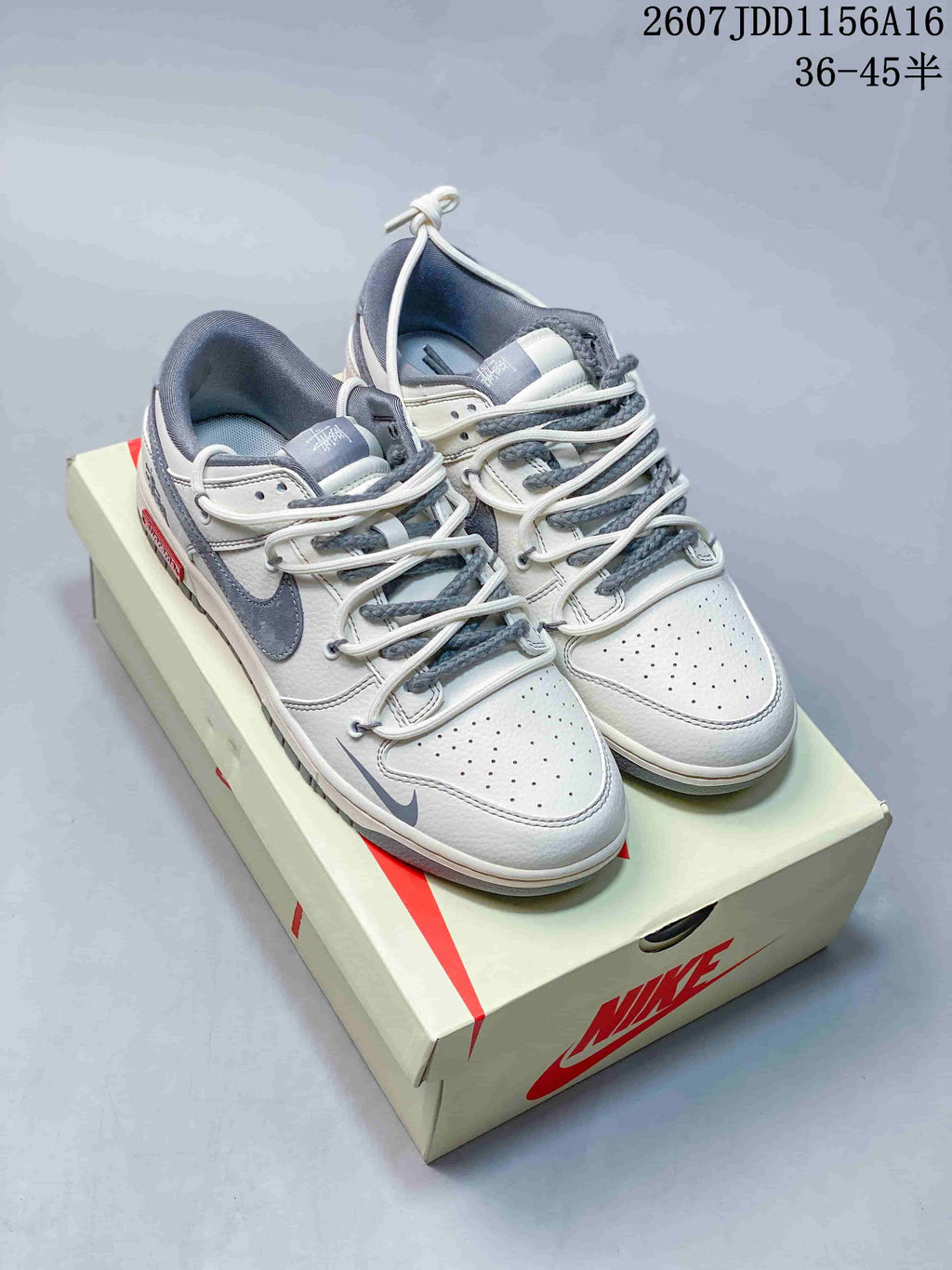 Pair of off-white and grey low-top sneakers displayed on a Nike-branded shoe box, with the source size range and code visible above.