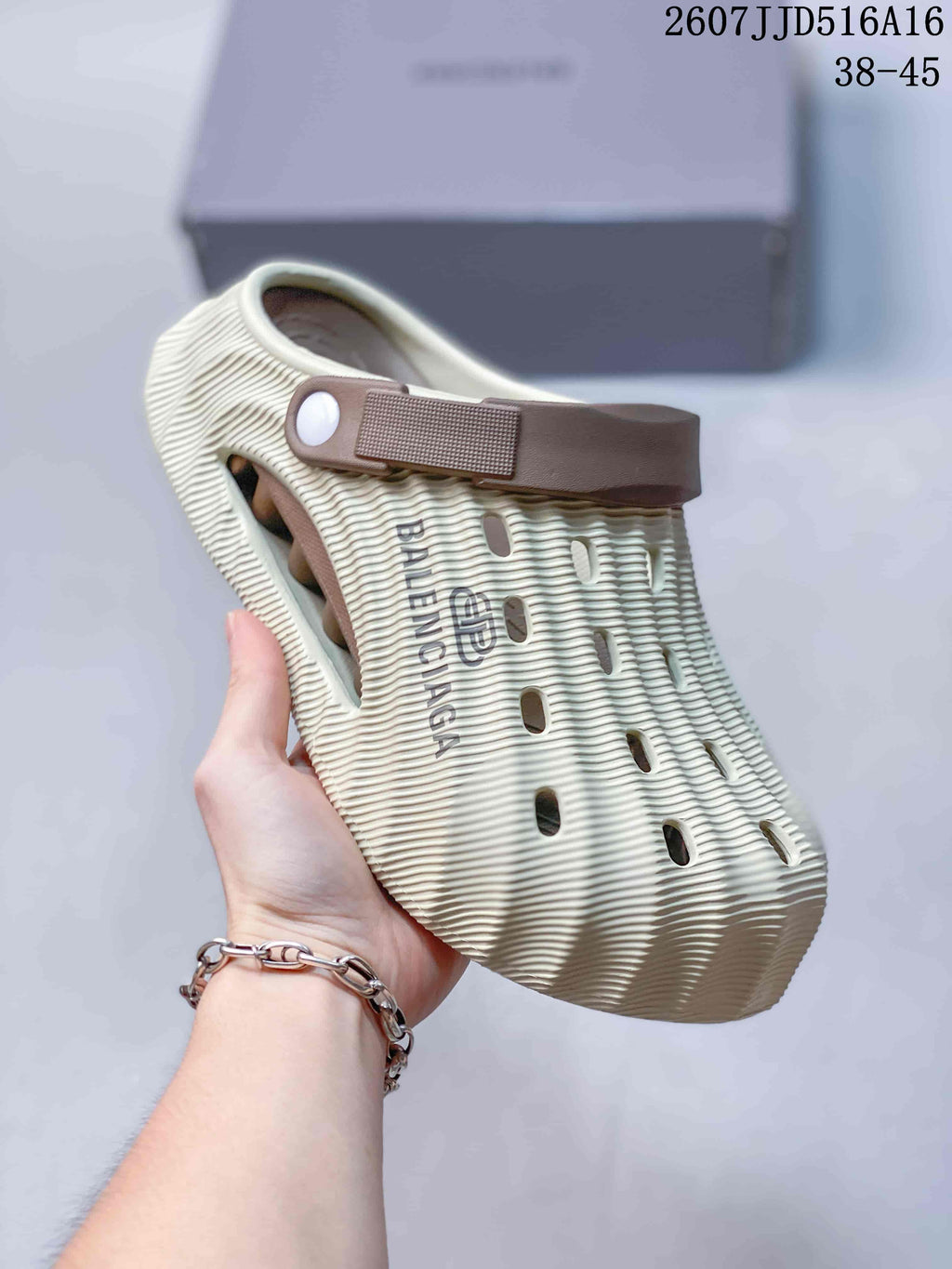 Angled side view of a cream clog slide showing the covered toe, ribbed construction, side branding, ventilation openings, and brown heel strap.
