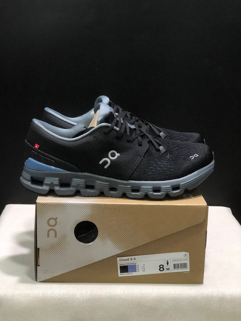 Side view of black On Cloud X4 shoes with gray segmented soles and blue heel accents.