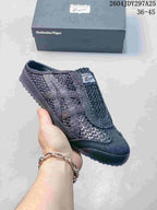 All-black Onitsuka Tiger Mexico 66 Sabot sneaker held in hand with its box behind it; the image shows style code 2604JDY297A25 and size range 36–45.