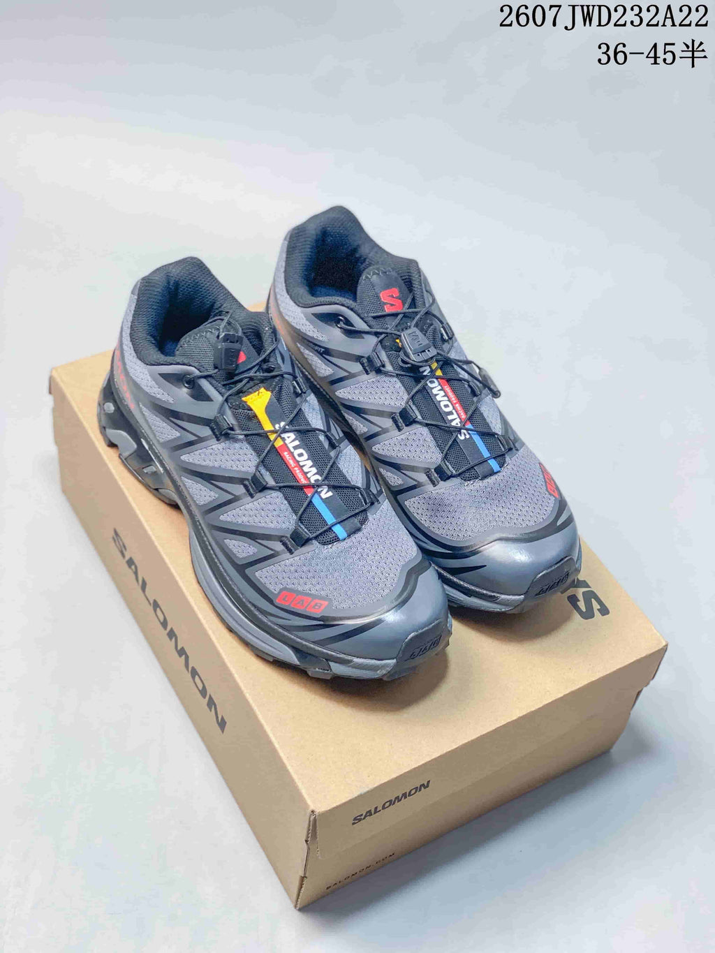 Pair of gray and black Salomon sneakers with red and blue accents displayed on a Salomon shoebox; overlay states 2607JWD232A22 and sizes 36–45.