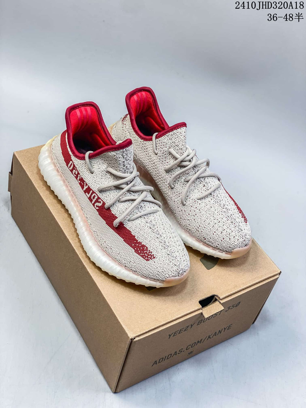 Pair of light knit Adidas Yeezy Boost 350 V2 sneakers with red accents displayed on a shoebox.