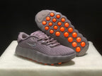Angled view showing the orange circular outsole elements beneath one sneaker.