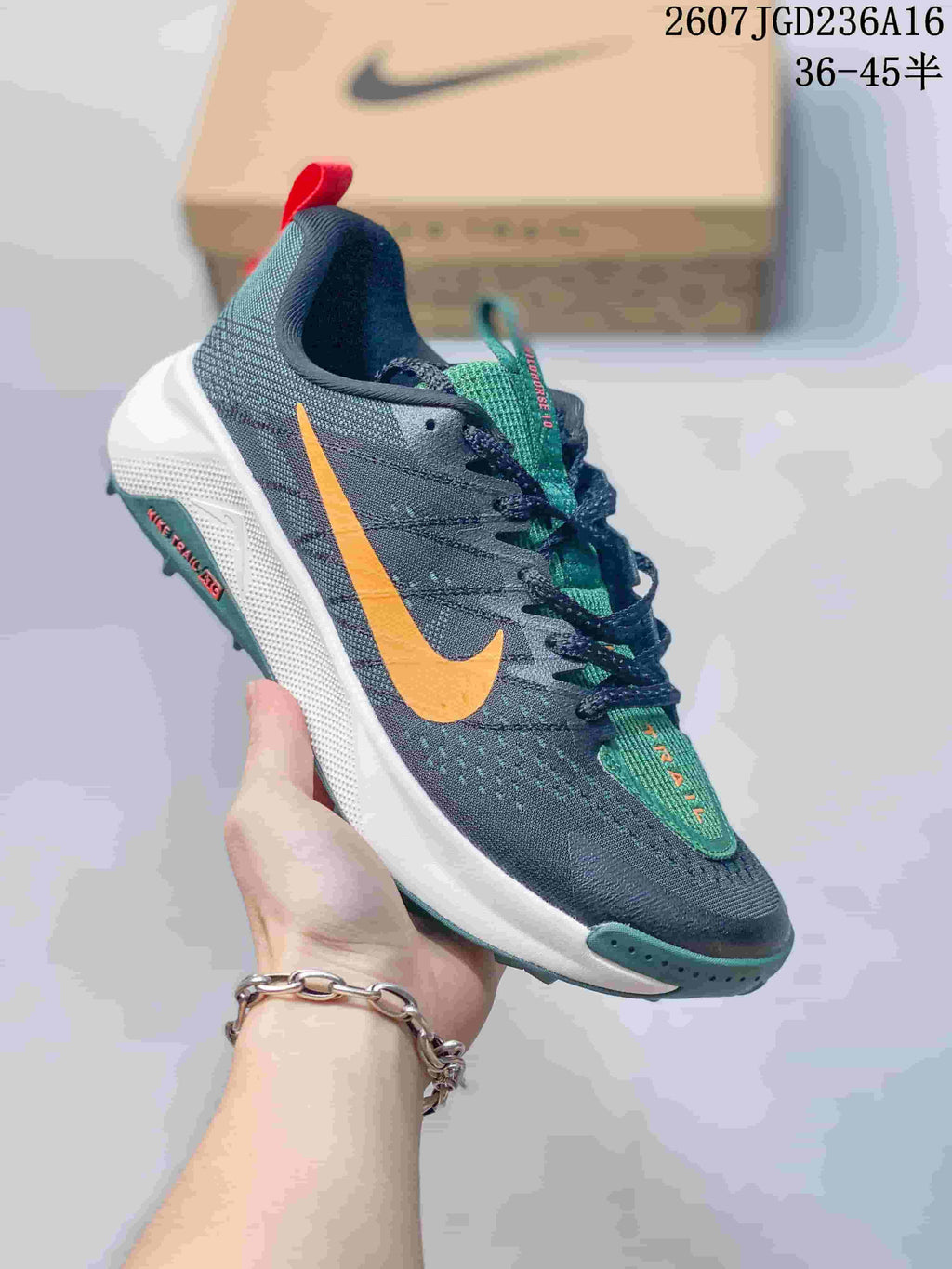 Angled side view of the sneaker showing the dark gray upper, large orange Nike Swoosh, white midsole, and green outsole details.