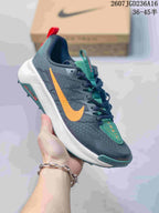 Angled side view of the sneaker showing the dark gray upper, large orange Nike Swoosh, white midsole, and green outsole details.