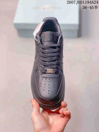 Top view of a black low-top sneaker showing the perforated toe box, woven laces and metallic lace ornament.