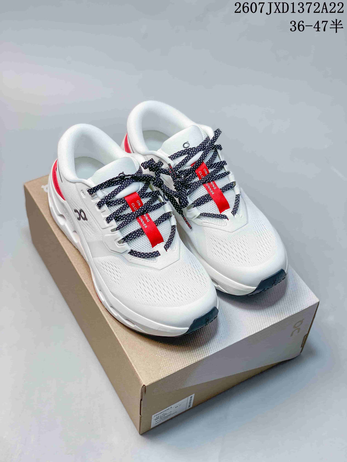 Pair of white On Cloudrunner 3 sneakers with red accents and black patterned laces displayed on a shoe box.