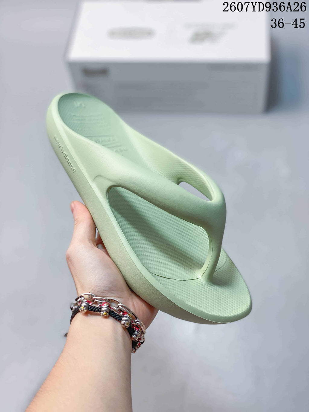 Angled view of a pale green New Balance thong sandal showing the textured footbed, open upper, and sidewall branding.