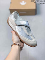 Close side view of a silver and white low-top sneaker with a wide strap, layered panels, and gum-style outsole.
