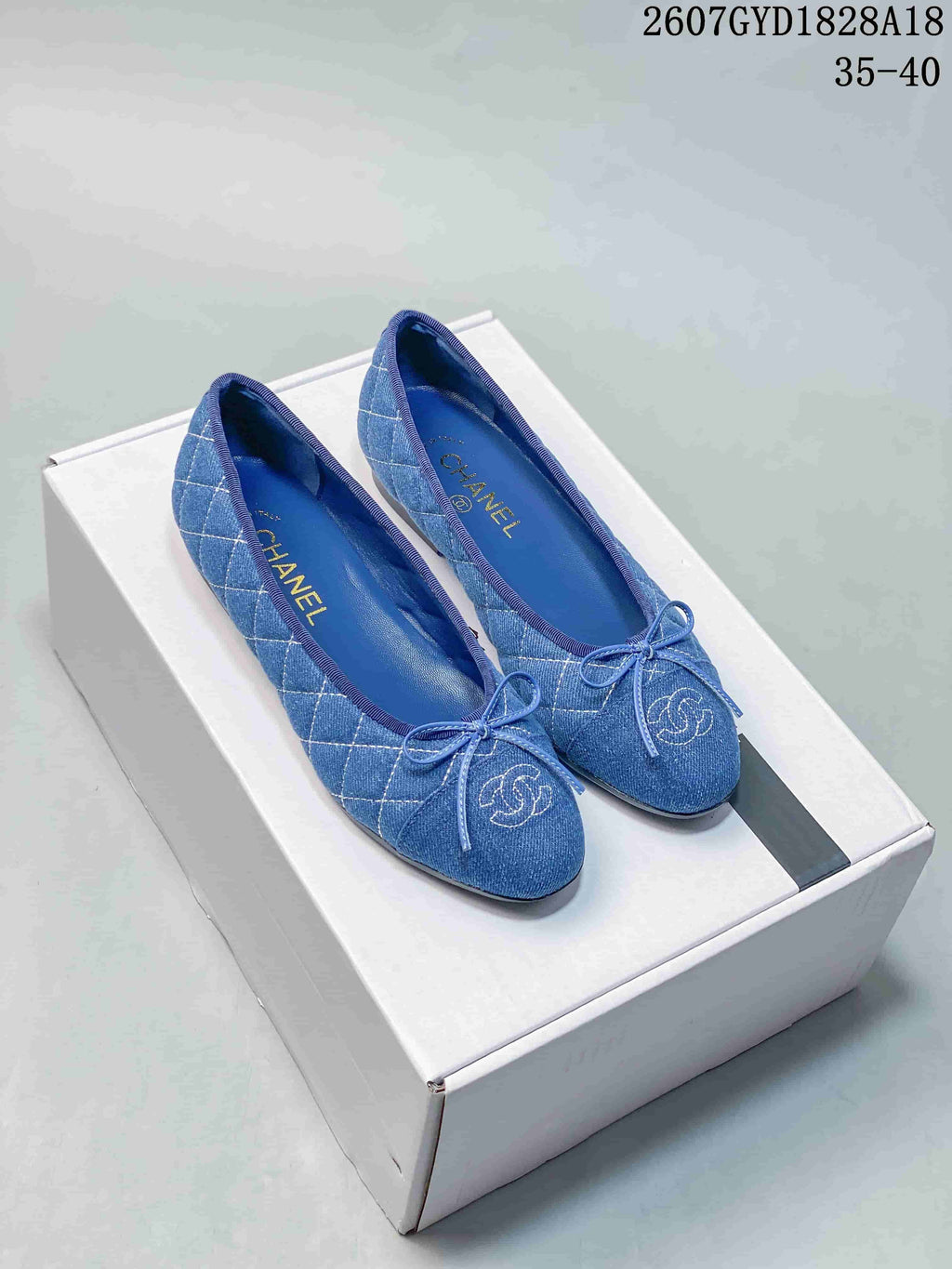 Blue denim-look quilted ballet flats with front bows and embroidered logo detailing on a shoe box.