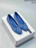Blue denim-look quilted ballet flats with front bows and embroidered logo detailing on a shoe box.