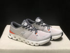 Three-quarter front view of the pair highlighting the silver uppers, dark laces, orange accents, and white soles.
