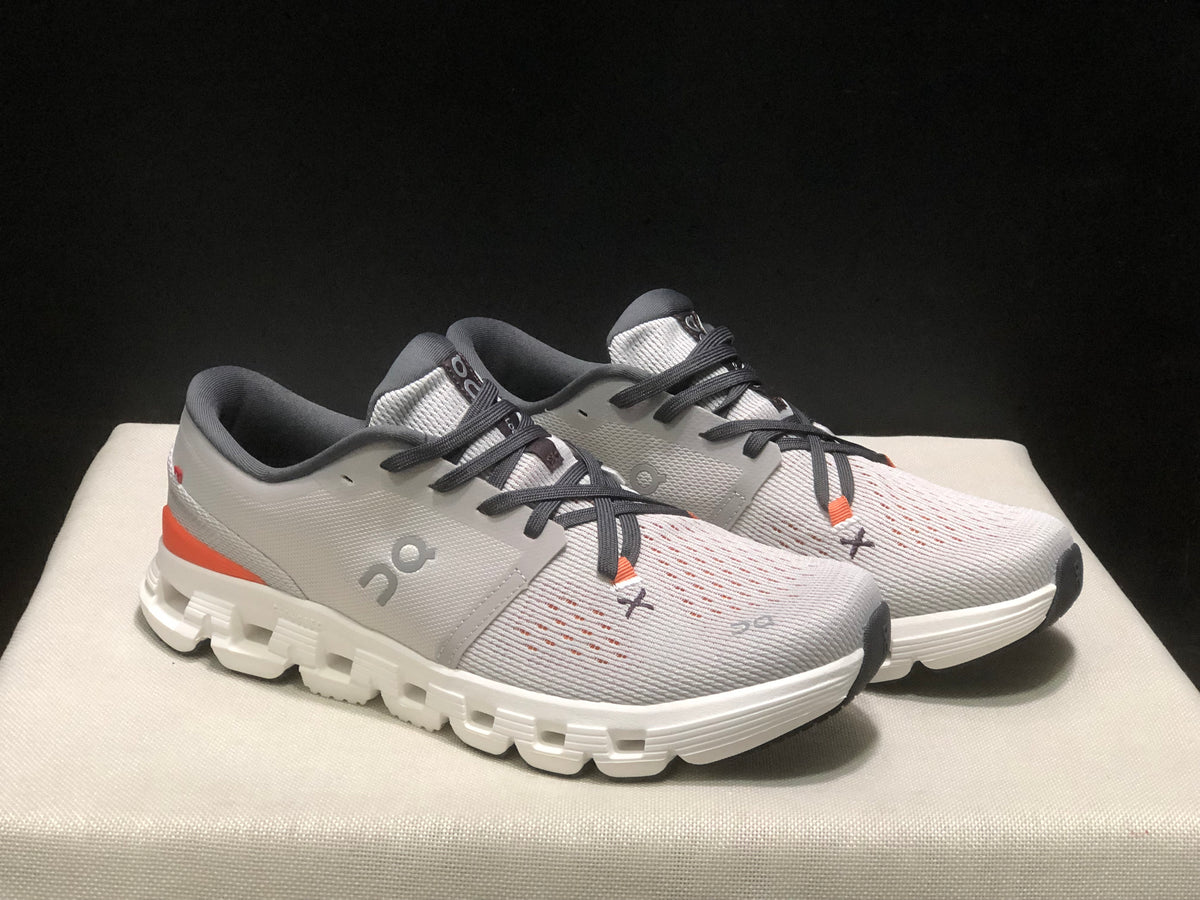 Three-quarter front view of the pair highlighting the silver uppers, dark laces, orange accents, and white soles.