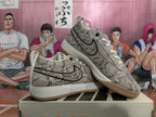 Angled view of a pair of gray patterned Nike Book 1 sneakers with black Swooshes, white midsoles, and gum-colored outsoles.