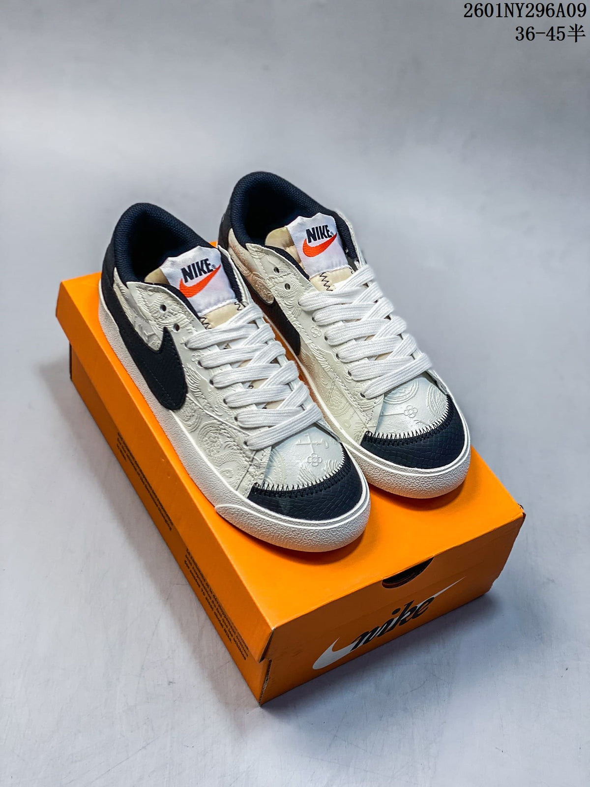 Pair of Nike Blazer Low '77 Jumbo sneakers shown from above on an orange Nike shoebox, with white uppers, black Swooshes, black toe panels, and orange tongue accents.