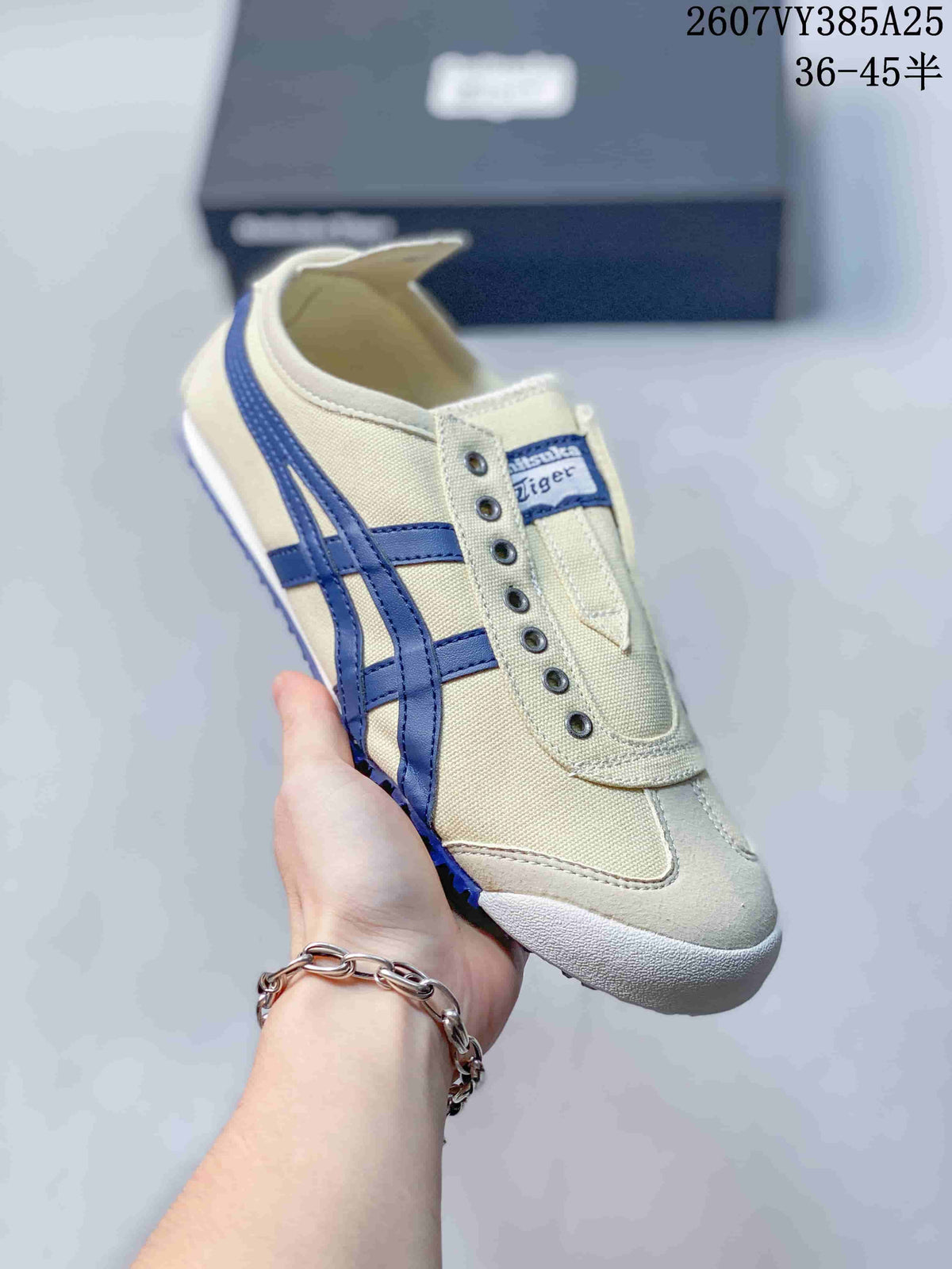 Angled close-up of the cream and blue sneaker showing the side stripes, slip-on opening, tongue label, and white toe bumper.