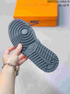 Close-up of the dark textured rubber outsole with circular traction patterns and embossed branding; an orange shoebox appears in the background.