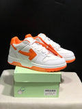 White and orange low-top sneakers displayed on a green shoe box, with the orange tag detail visible.