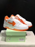 White and orange low-top sneakers displayed on a green shoe box, with the orange tag detail visible.