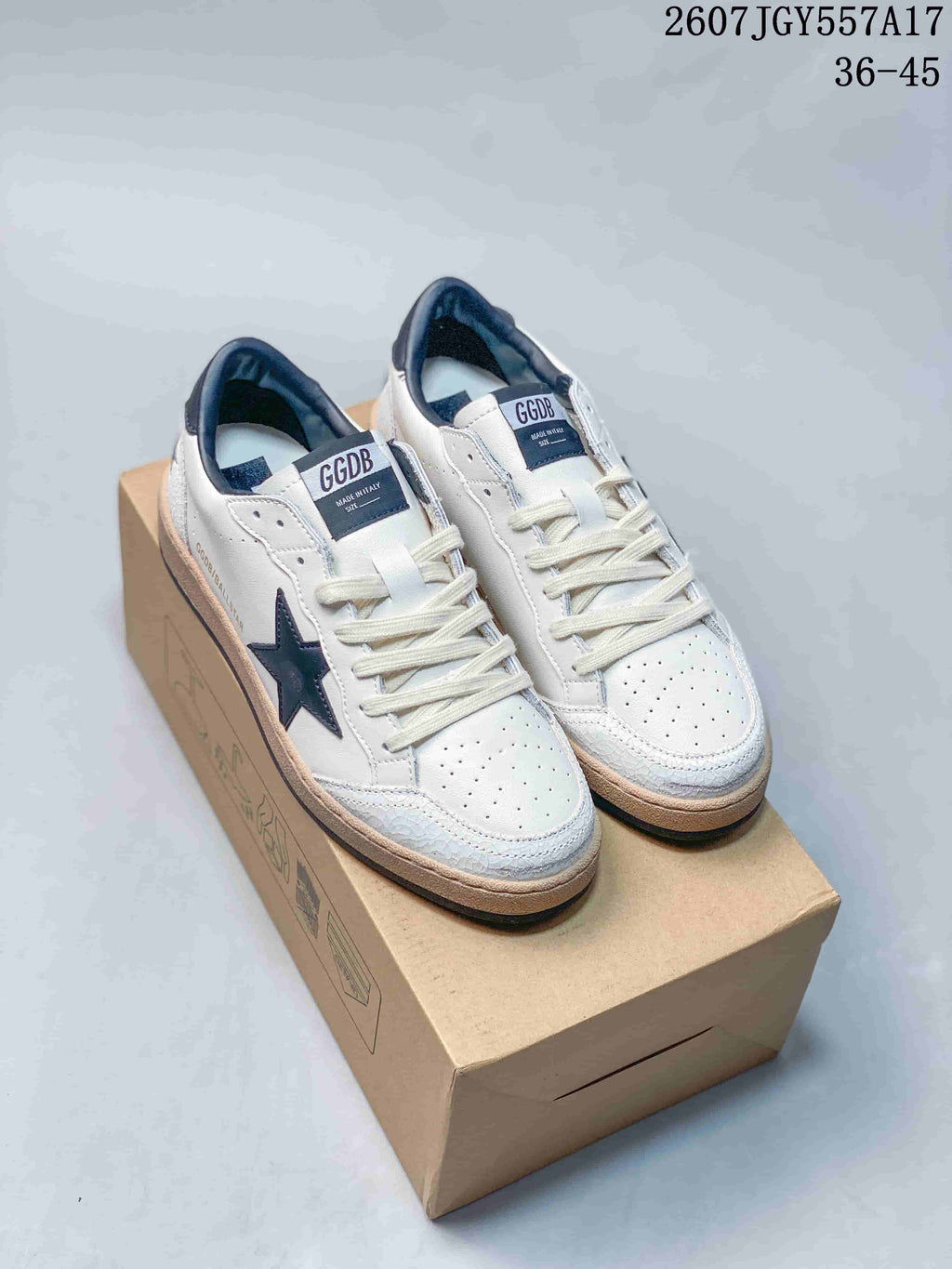 Pair of white Golden Goose Ball Star sneakers with navy stars displayed on a shoebox; style code 2607TGY557A17 and size range 36–45 are visible.