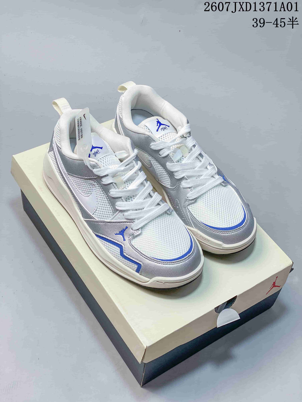 Pair of white and silver Jordan CMFT Era low-top sneakers with blue accents, displayed on a shoebox.