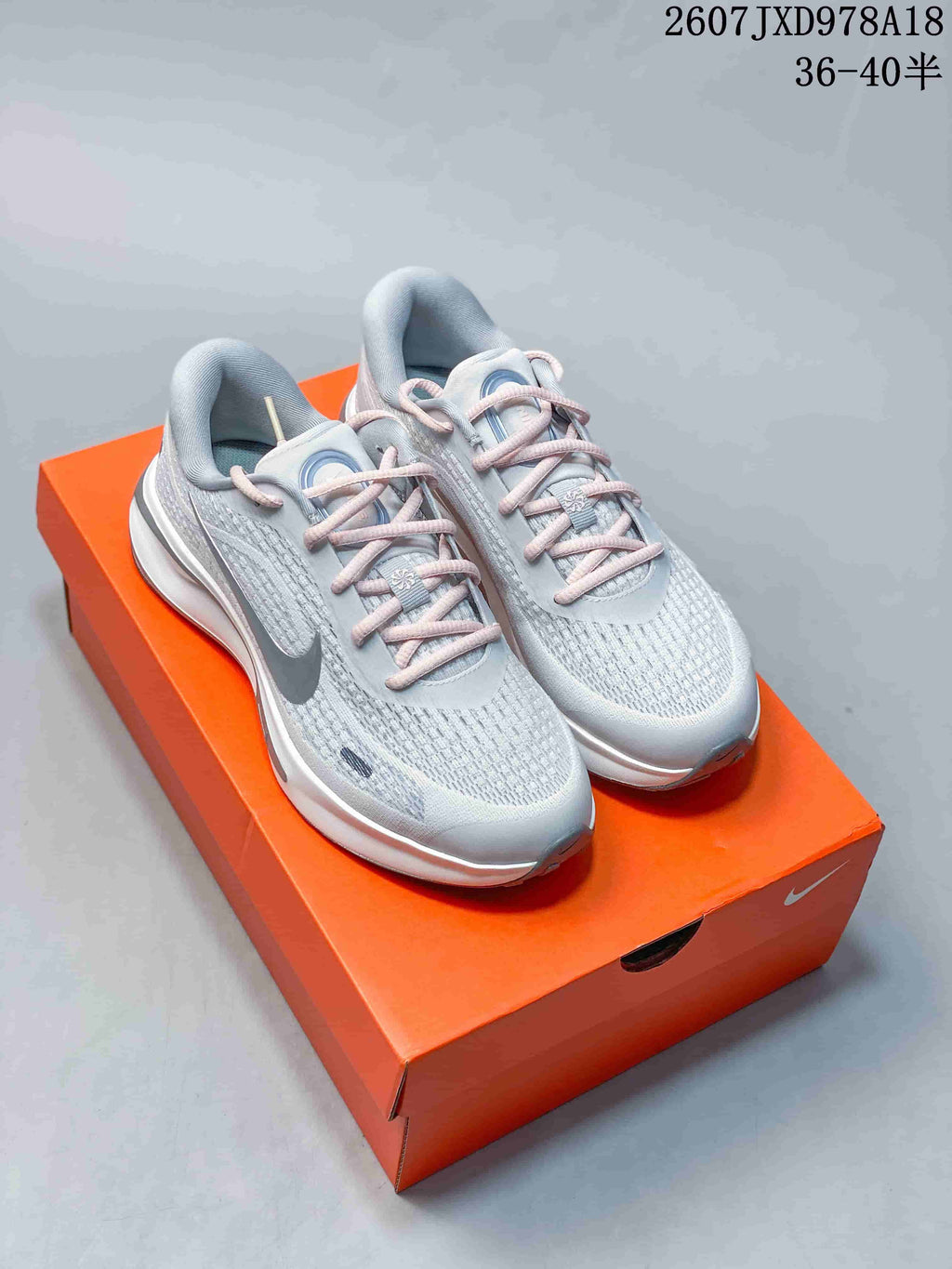 Pair of light gray Nike Journey Run shoes with pink laces displayed on an orange shoebox; visible text shows style code 2607JXD978A18 and size range 36–40.