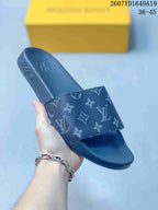 Angled view of a navy monogram slide sandal showing the wide strap, open toe, raised sole, and branding on the footbed.