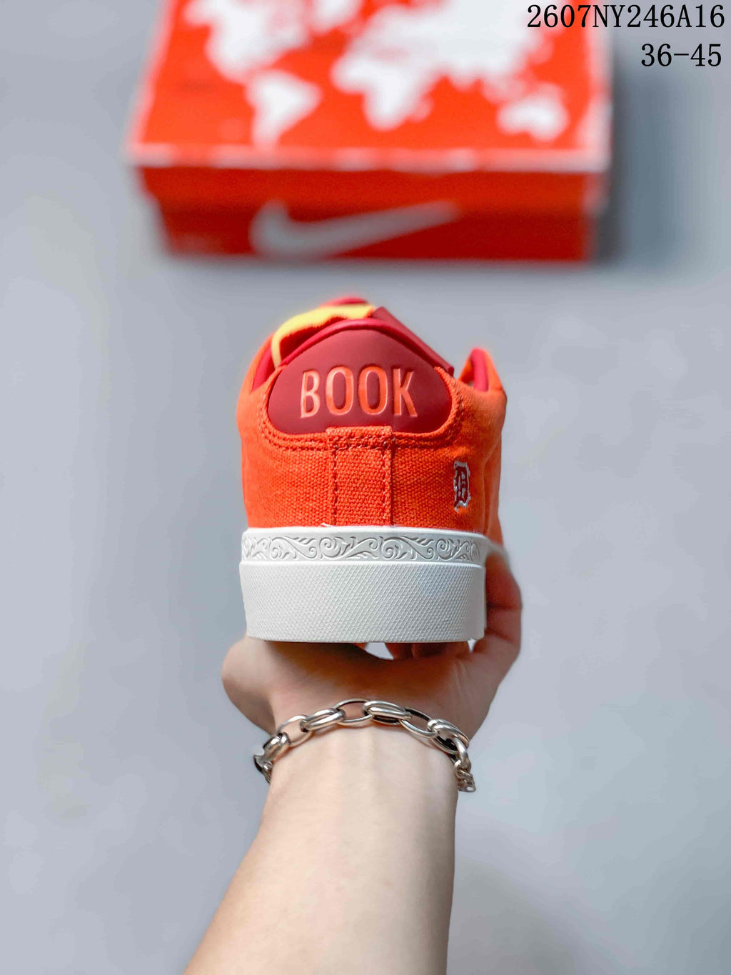 Rear view of the orange sneaker showing BOOK lettering, a small side emblem, and decorative white midsole detailing.
