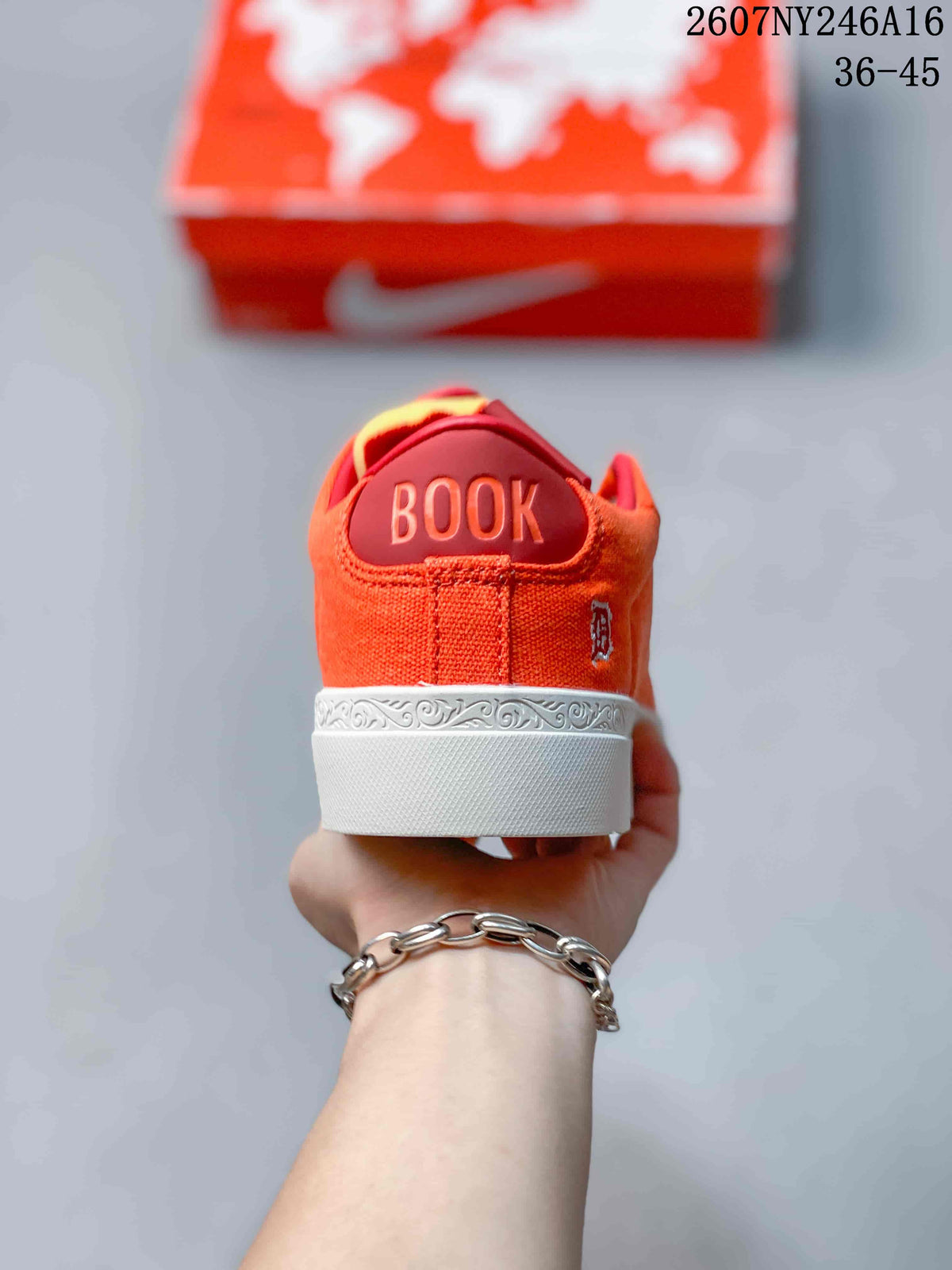Rear view of the orange sneaker showing BOOK lettering, a small side emblem, and decorative white midsole detailing.