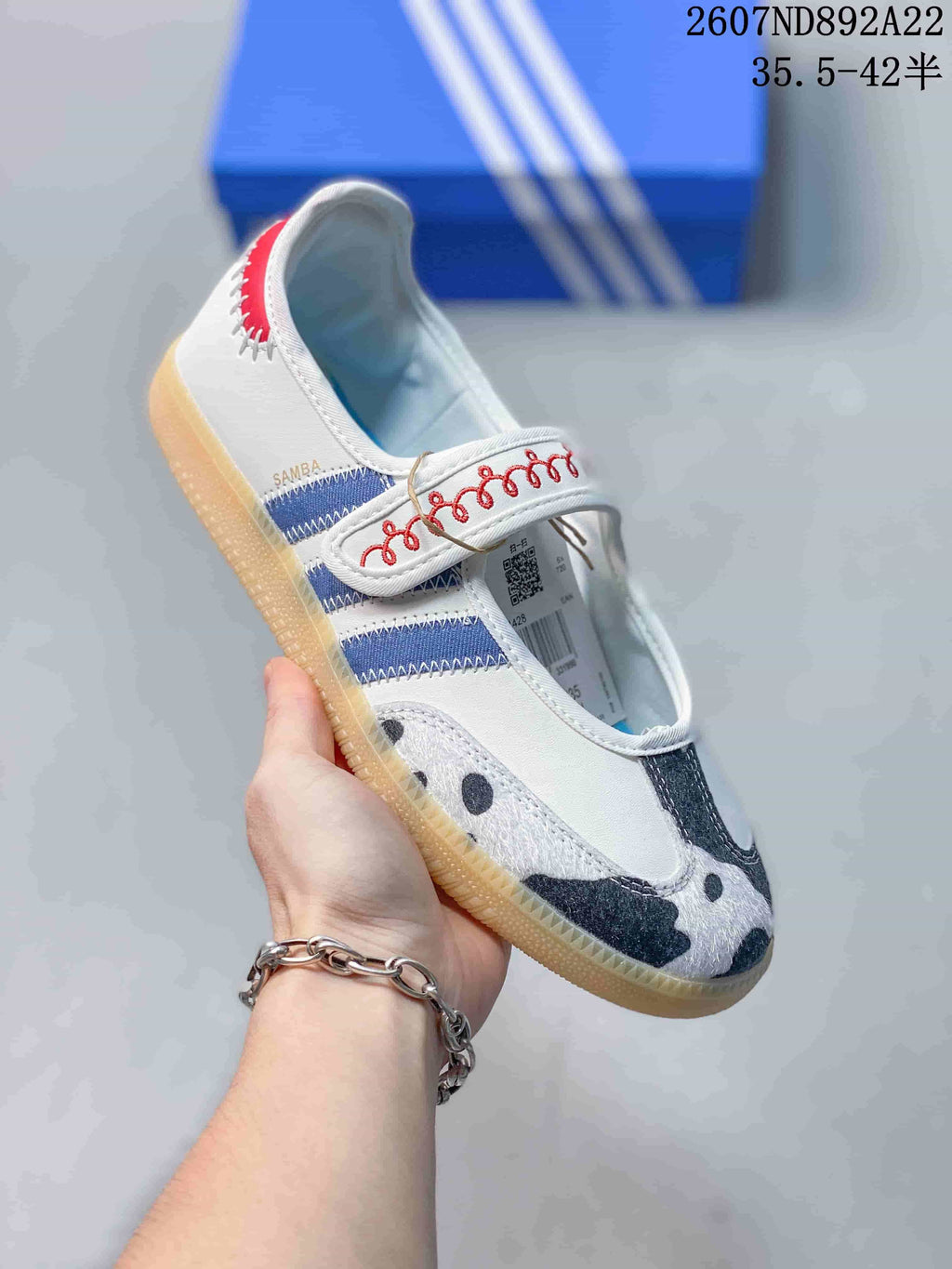 Angled side view of the adidas Samba Jane sneaker showing the strap, blue stripes, red detailing, patterned toe, and visible SAMBA text.