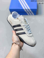 Angled side view of the white adidas sneaker showing black side stripes, gold-toned side branding, and a dark outsole.