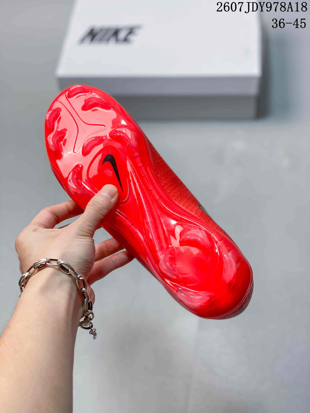 Underside view of a red soccer cleat showing the translucent red studded outsole and black Nike swoosh.