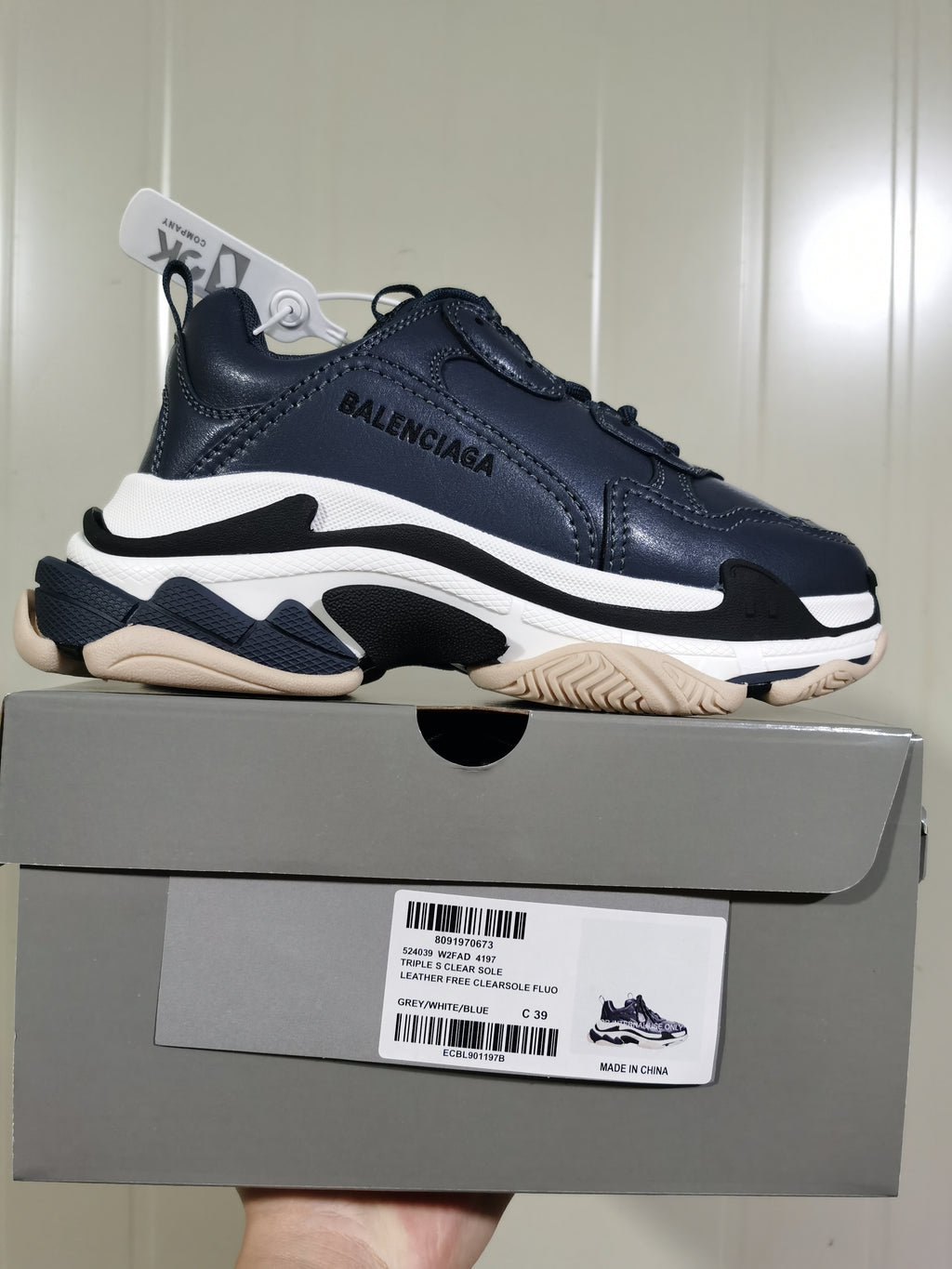 Balenciaga Triple S sneaker in dark blue-grey, white, black, and beige tones displayed on its box; the box label shows size C39 and style details.