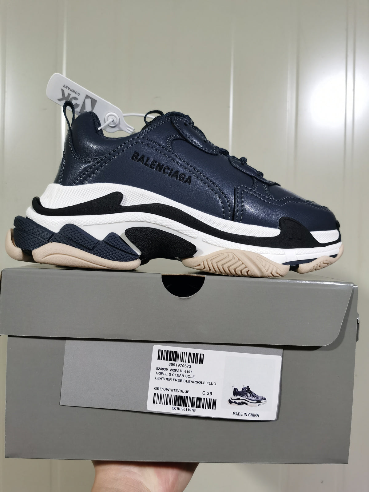 Balenciaga Triple S sneaker in dark blue-grey, white, black, and beige tones displayed on its box; the box label shows size C39 and style details.