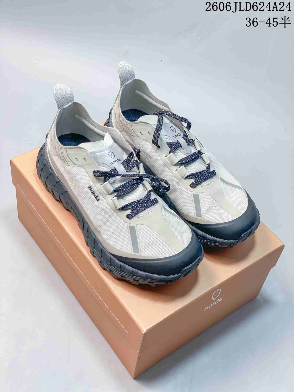 Pair of light gray and off-white Norda hiking shoes with dark laces on a Norda box.