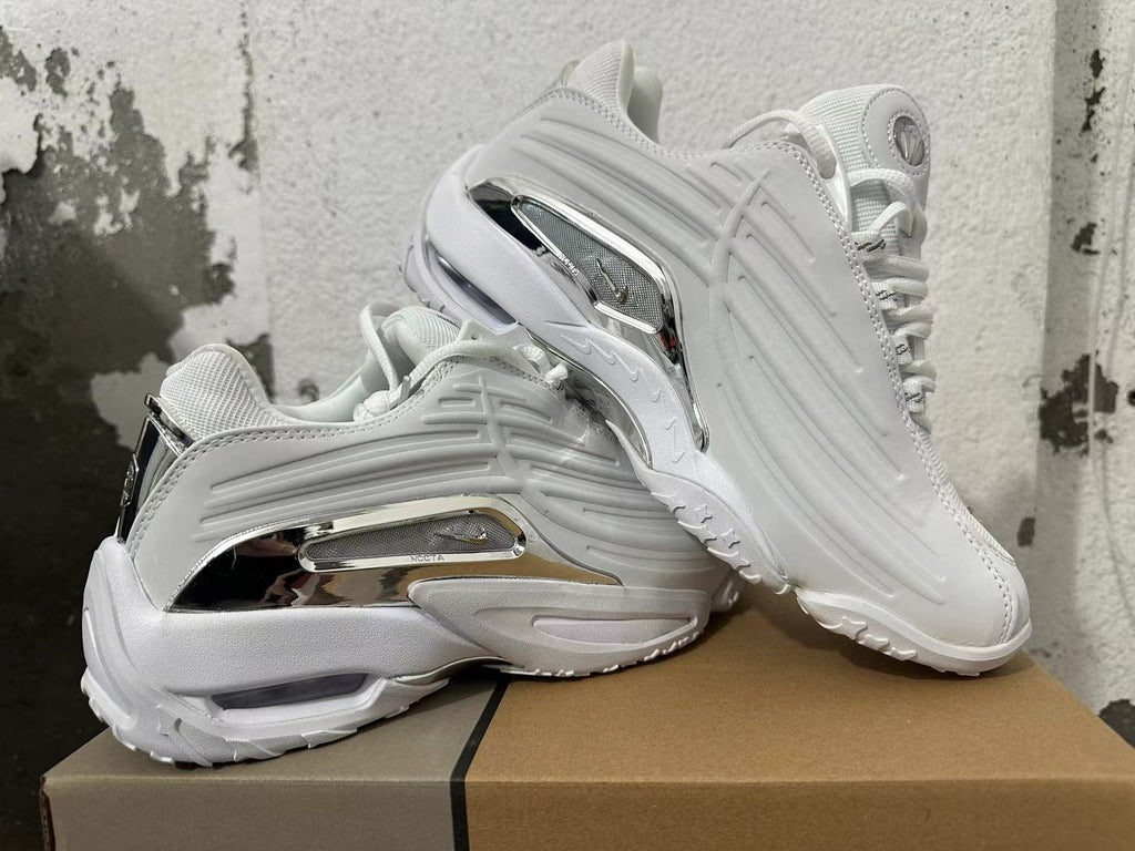 Pair of white Nike NOCTA Glide sneakers shown at an angle, highlighting the sculpted sides and silver-tone accents.