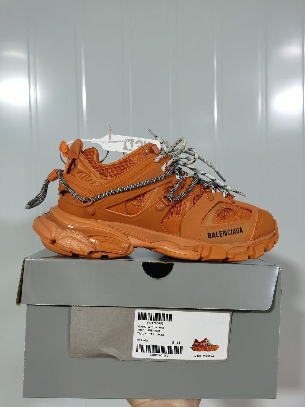 Side view of the orange Balenciaga Track 7000 sneaker resting on its box; the label identifies the Track sneaker, orange color, and sample size E 41.