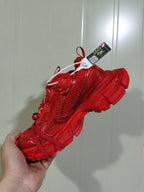 Close-up side view of a red monochrome sneaker showing the textured upper, layered panels, side Swoosh design, and red laces.