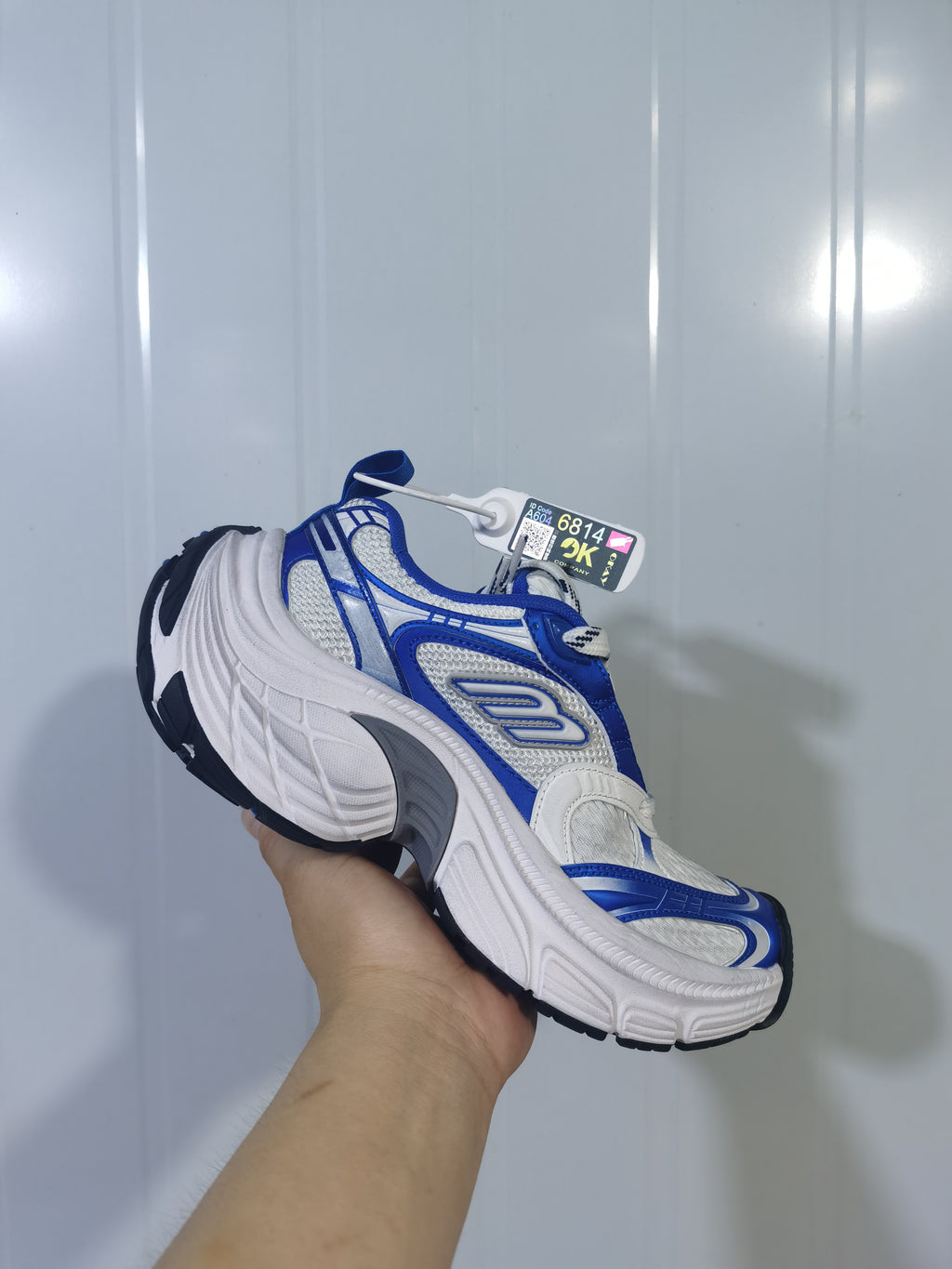 Angled view of the white and royal blue sneaker highlighting the lace-up front, mesh-like upper sections, and contrasting overlays.