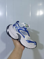 Angled view of the white and royal blue sneaker highlighting the lace-up front, mesh-like upper sections, and contrasting overlays.