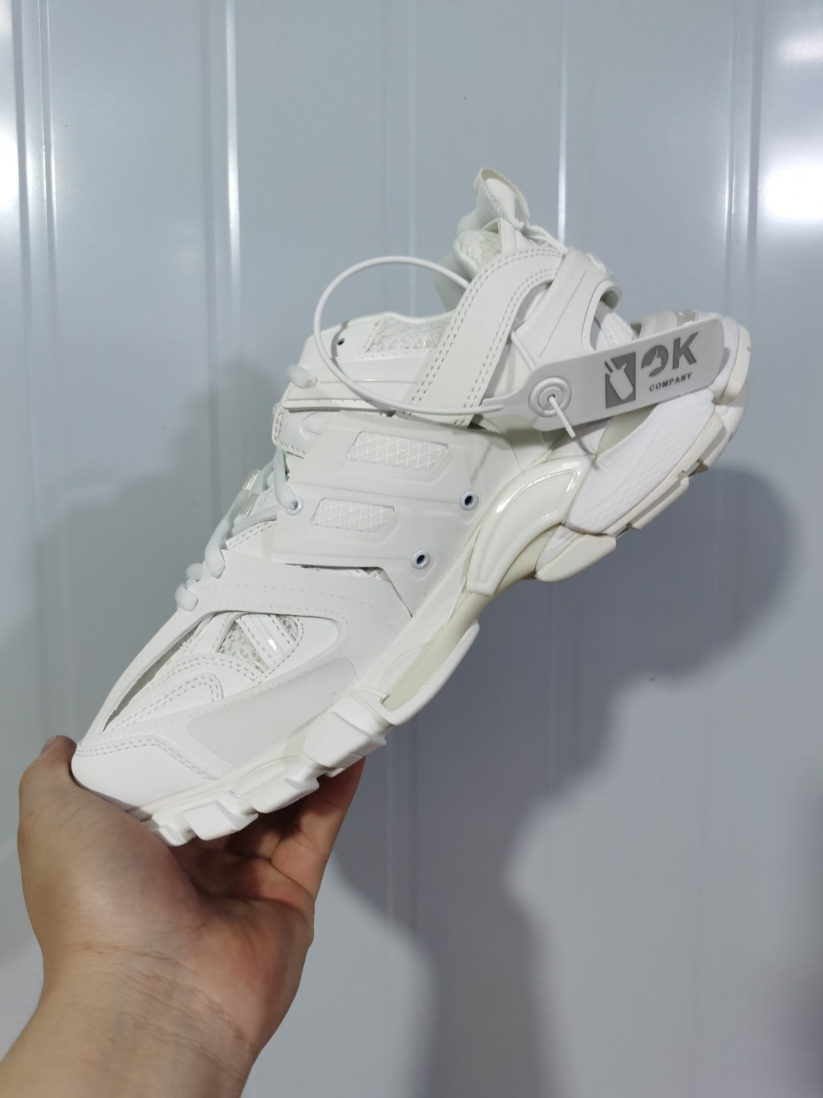 White and black Balenciaga Track sneaker held at an angle, showing the layered upper, lace fastening and segmented sole.
