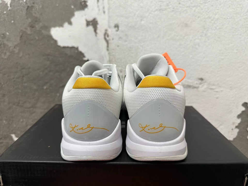 Rear view of white Nike Kobe basketball shoes with yellow heel tabs and signature details.