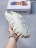 Close side view of a white covered-toe slide with perforated detailing and a raised textured sole edge.