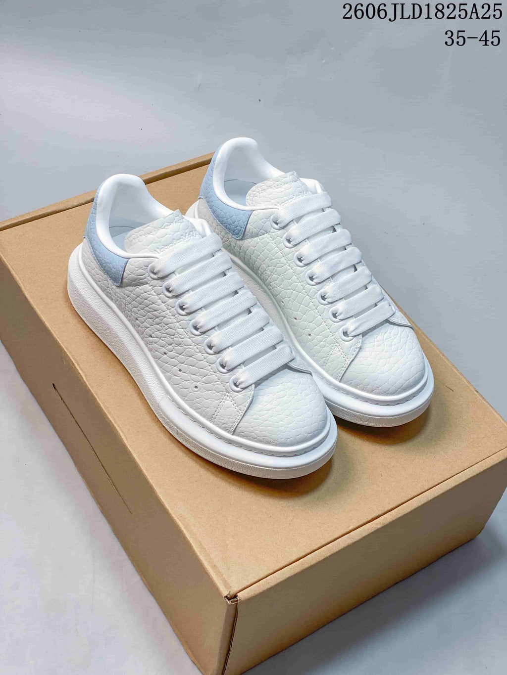 Pair of white textured platform sneakers with pale blue heel panels, shown on a box.