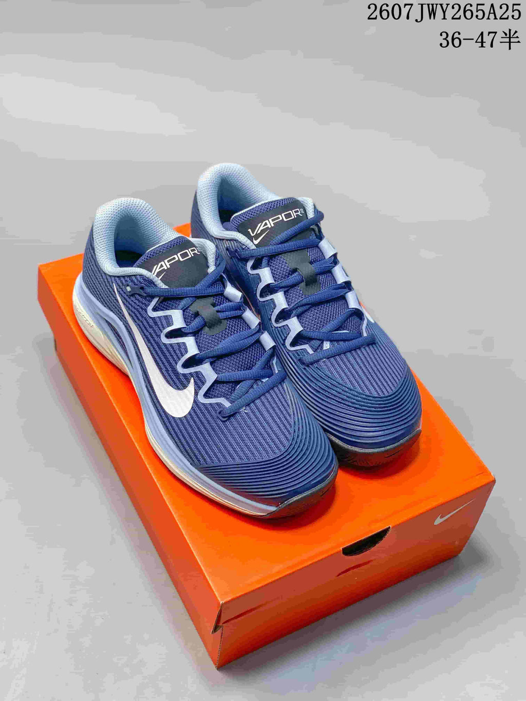 Pair of navy and white Nike Vapor 12 low-top tennis shoes displayed on an orange shoe box; overlay text shows style code 2607JWY265A25 and size range 36–47.5.