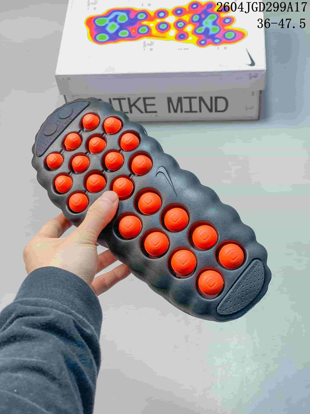 Underside view of a Nike Mind slide showing the sculpted dark outsole and multiple contrasting orange traction nodes.