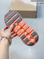 Underside view of the pink and coral sneaker showing segmented dark outsole sections and open channels in the midsole.