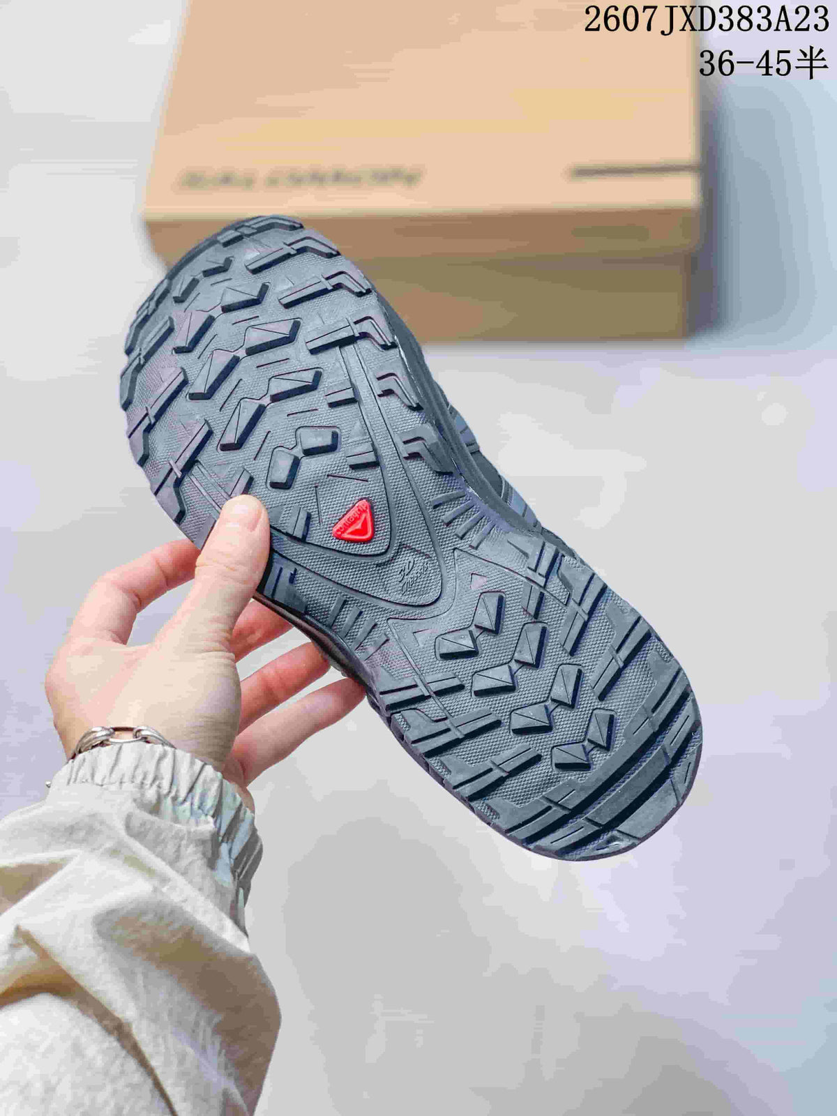 Close view of the gray sneaker outsole showing a deep, directional lug pattern and a red Salomon detail.