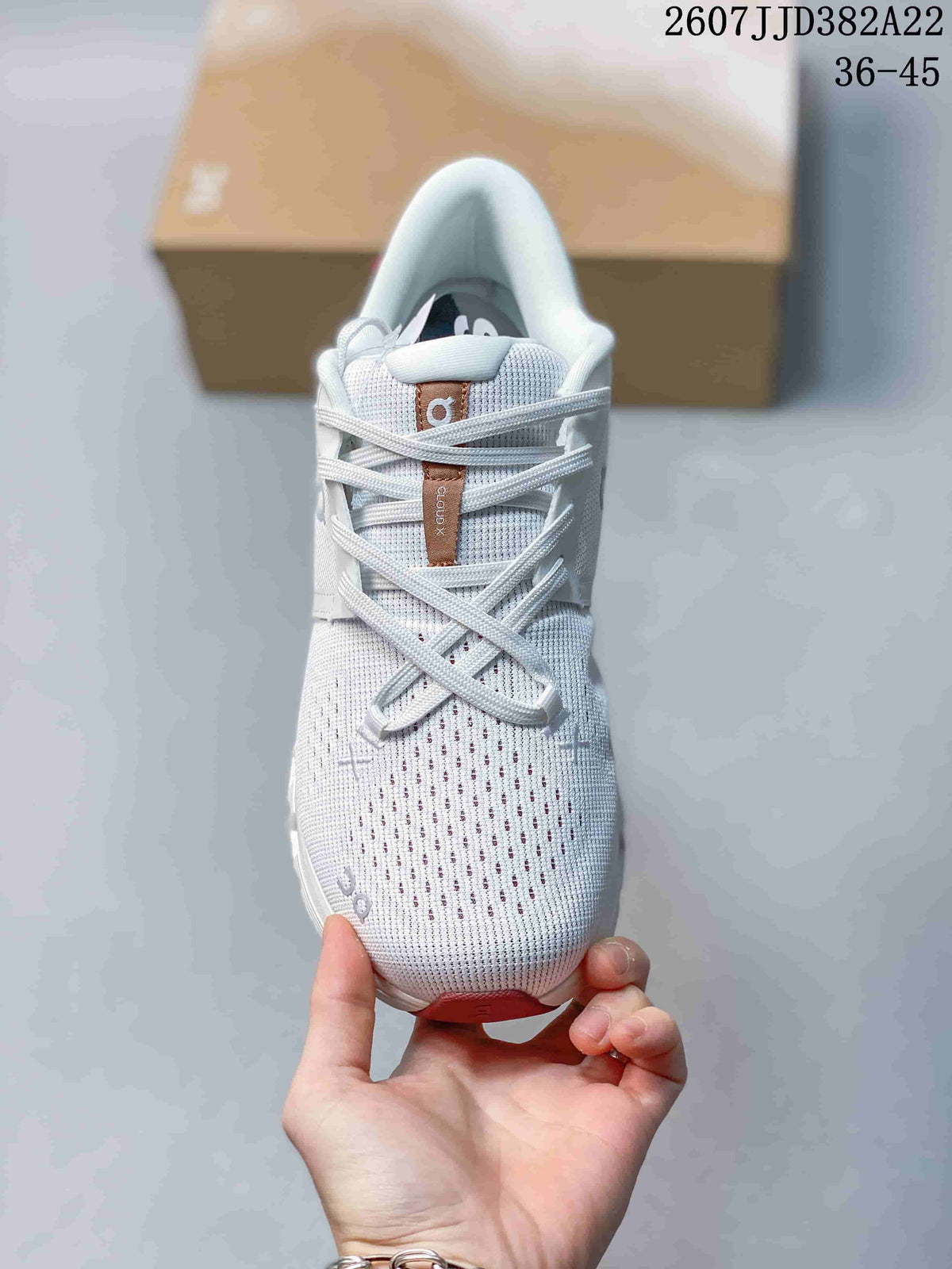 Front view of the white sneaker showing the perforated knit-style toe box, crossed laces, tongue label, and pink outsole accent.