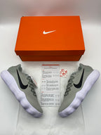 Grey Nike sneakers with black Swoosh logos and white ridged soles beside an orange shoe box